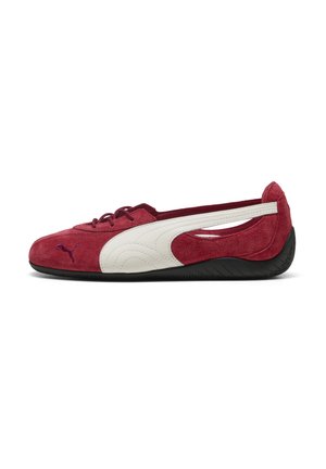 Plochá červená semišová bota s černou podešví, bílým bočním pruhem a malým logem Puma na špičce, zobrazená z vnější strany.