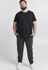 Crna pamučna majica uparena sa sivim trenirkama. Trenirka ima meku teksturu i elastične rubove. Bele patike upotpunjuju outfit.