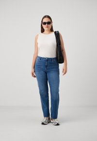 Blue jeans with a straight-leg fit, paired with a white ribbed tank top. A black pleated bag is slung over the shoulder, and sunglasses are worn.