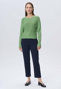 Zielony sweter z teksturowanym splotem, dekolt łódka, w połączeniu z granatowymi, dopasowanymi spodniami oraz czarnymi butami wsuwanymi. Prosty, nowoczesny design.