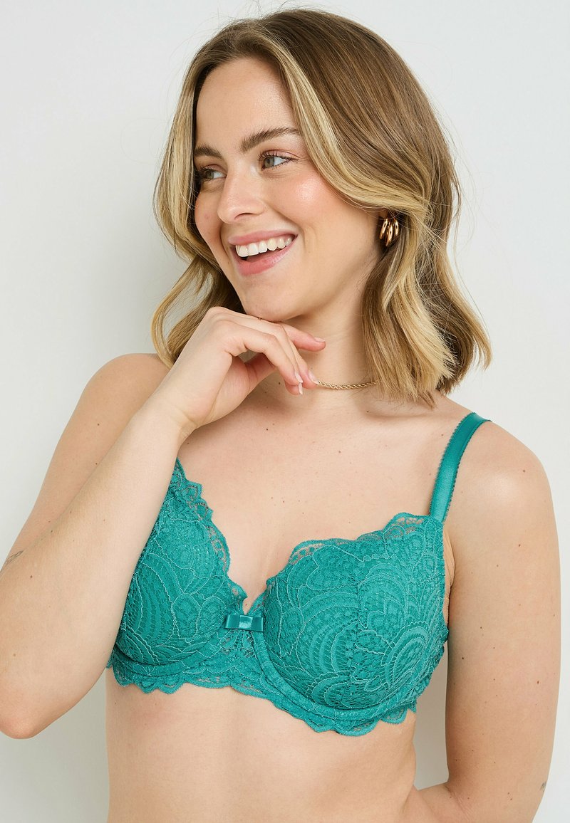 Reggiseno in pizzo color teal con motivo floreale, dotato di coppe imbottite, bordi ondulati e un piccolo dettaglio a fiocco al centro. Spalline regolabili.