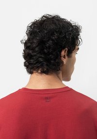 T-shirt en coton bio rouge avec un col rond et une étiquette visible au dos. Texture douce avec un design simple.