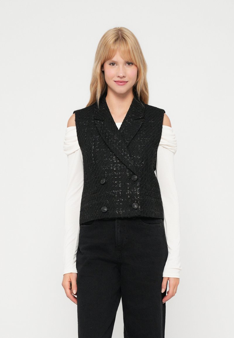 Crni skraćeni dvoredni prsluk od teksturirane tkanine, s velikim dugmadi i klasičnim reverima. Nosiv preko bijele majice dugih rukava.