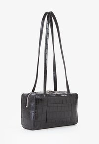 Borsa nera in pelle stampata a forma di coccodrillo con forma rettangolare, chiusura con zip argentata e due sottili manici per il trasporto.