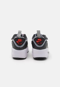 Nike Air sneaker, fekete és szürke dizájnnal, fehér középtalppal és piros logóval a saroknál. Texturált szövet felsőrész és fülecskék kiemelések.