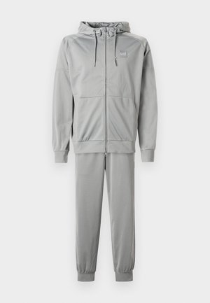 Haut à zip gris et pantalons assortis en tissu lisse, avec une capuche, des poignets côtelés, et un petit logo sur la poitrine.
