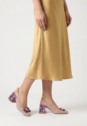 Benedenlichaam met een gouden satijnen midi-rok en roze suède blockhakken met een paarse bloemenpatroon gesp en hiel detail.