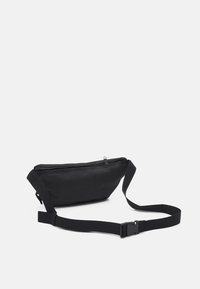 Borchia in tessuto nero con una texture liscia, chiusura con zip e cintura regolabile. Design elegante senza loghi o motivi visibili.