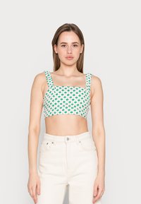 Top cropped com decote quadrado, estampado floral verde sobre um fundo creme, alças largas, combinado com jeans de cintura alta em denim claro.