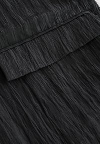Tissu noir avec un motif texturé et froissé. Détail de rabat en haut. Le matériau semble léger et légèrement brillant.