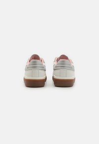 Des sneakers avec une tige blanche et argentée, un doublure rose et une semelle en caoutchouc marron. Forme arrondie avec une texture lisse et des détails de couleur contrastants.
