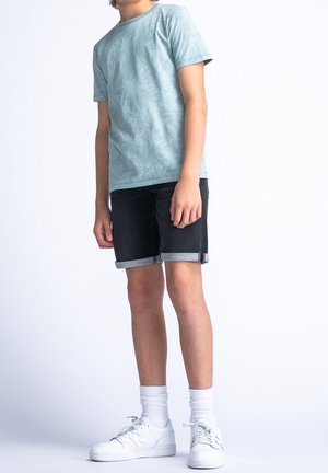 Lichtblauw T-shirt met een textuur patroon, gecombineerd met zwarte denim shorts met opgerolde zomen, en witte sneakers met grijze sokken.