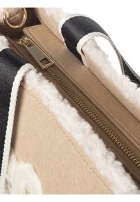 Beige tas met een gestructureerde buitenkant met een pluizige rand, gouden ritshardware en zwart-witte bandaccenten.