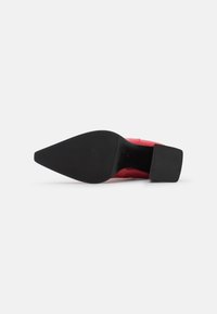 Chaussure à talon haut rouge avec un bout pointu, présentant un cuir lisse sur le dessus et une semelle en caoutchouc noir texturé, affichant un design solide.