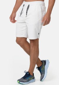 Hvide shorts med elastisk talje og snoretræk, sidelommer og et lille mærke. Sammen med grå sneakers med grønne detaljer.