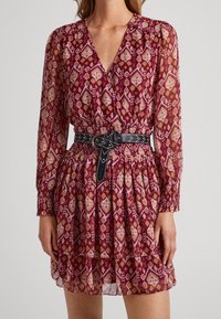 Rotes und pinkfarbenes gemustertes Kleid mit langen Ärmeln, einem tiefen V-Ausschnitt und gerafftem Taillenbund. Es hat einen schwarzen Gürtel mit dekorativen Nähten.