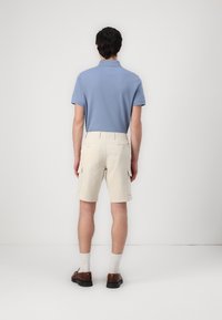 Tricou polo de culoare bleu deschis, pantaloni scurți cargo bej, pantofi maronii și șosete albe. Tricoul are mâneci scurte; pantaloni scurți au buzunare laterale și curea.