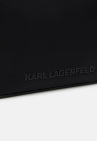 Černý textilní povrch s vyraženým logem "KARL LAGERFELD" ve shodné černé barvě blízko spodního okraje.