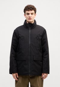 Giacca nera isolante con colletto alto, zip frontale, due tasche al petto e due tasche inferiori. Tessuto liscio, opaco e design senza decorazioni.