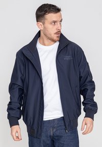 Marineblauer Bomberjacke aus leichtem Stoff mit hohem Kragen, gerippten Bündchen und dezenten Logodetails. Mit Reißverschlusstaschen an den Seiten.