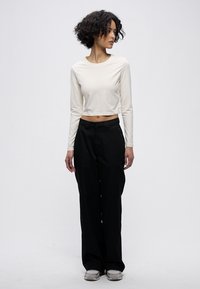 Hvit langermet crop-top kombinert med svarte vide bukser. Antrekket har et minimalistisk design og et glatt, mykt stoff.