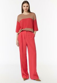 Czerwona i beżowa bluzka z kolorowymi блоками, z krótkim rękawem, zestawiona z czerwonymi spodniami o wysokim stanie i szerokimi nogawkami oraz spiczastymi beżowymi szpilkami.