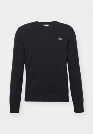 Schwarzer V-Ausschnitt-Pullover aus weichem Stoff, mit langen Ärmeln und einem kleinen grünen gestickten Logo auf der Brust.