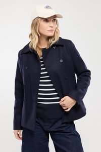 Manteau croisé en mélange de laine bleu marine avec de grands boutons, un col chemise et des poignets boutonnés, associé à un haut rayé et un denim.