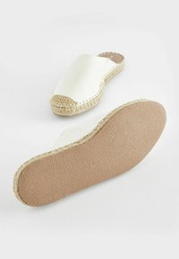 Vit slip-on espadrille med rund tå, jute-detaljer på ovandelen och texturerad gummisula. Slät material och minimalistisk design.