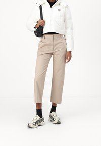 Vit vadderad jacka med kort skärning, kombinerad med ljusbeige, skräddarsydda, korta byxor. Svarta strumpor och beige-svarta sneakers kompletterar outfiten.