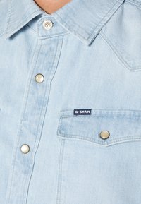 Jasnoniebieska koszula dżinsowa z kołnierzykiem na spiczasto, srebrnymi zatrzaskami i kieszenią na piersi z metką G-Star. Miękka faktura i casualowy design.