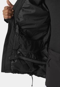 Interior de chaqueta negra con material de nylon suave, ajustador de cordón, bolsillo con cremallera y bolsillo de malla con un patrón de lunares.