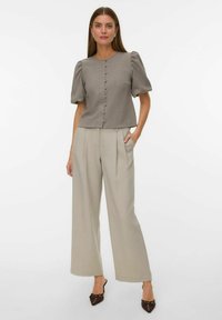 Siva skraćena bluza s naboranim rukavima i gumbima sprijeda, uparena s laganim bež širokim hlačama i tamnim sandalama s petom.