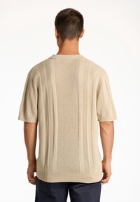 Beige stickad kortärmad tröja med vertikal ribbning och avslappnad passform, med en rundad halsringning och en något längre bakre fåll.