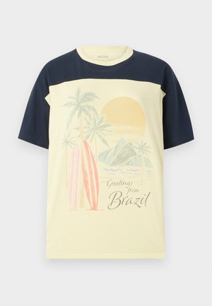 T-shirt giallo chiaro con maniche blu navy. Presenta una stampa grafica di palme, tavole da surf e un sole, accompagnata dal testo "Saluti dal Brasile".