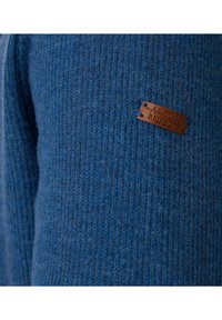 Blauwe geribbelde trui gemaakt van zachte gebreide stof, voorzien van een rechthoekig bruin leren label dat is bevestigd en geperst met "Authentic Clothing REDMOND."