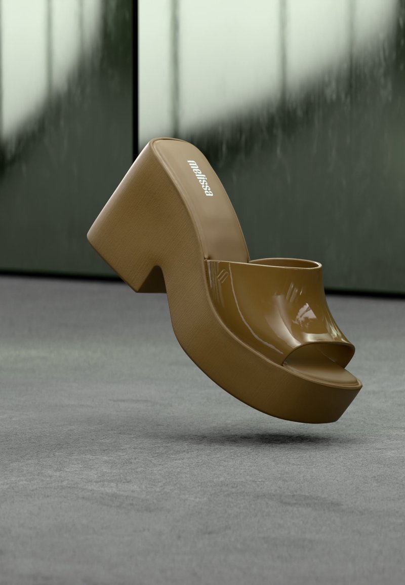 Καφέ πλατφόρμα σανδάλι με ανοιχτά δάχτυλα, χοντρό τακούνι και λογότυπο "melissa" στην εσωτερική σόλα, εμφανίζεται μπροστά σε θολό πράσινο και γκρι φόντο.