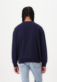 Sudadera azul marino con un ajuste relajado, cuello redondo y puños acanalados. Presenta una textura suave y un diseño simple y limpio.