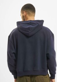 Felpa con cappuccio blu navy, in tessuto pesante, taglio rilassato, polsini e orlo a coste, con cappuccio foderato e dettagli minimi.