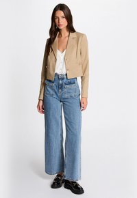 Geknipt beige streepjasje over een witte blouse, gecombineerd met lichtblauwe, hoog- taille, wijde jeans en zwarte platform loafers.