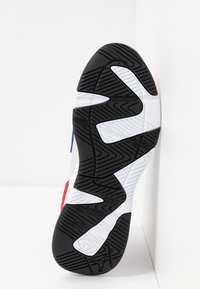 Semelle d'une chaussure de sport avec un motif en zigzag noir et blanc, montrant une bande de roulement en caoutchouc texturé conçue pour l'adhérence.