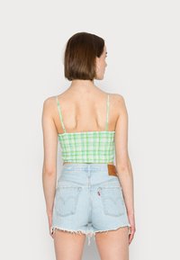 Top cropped xadrez verde e branco com alças ajustáveis, combinado com calções de ganga azul claro desfiados, com uma etiqueta de couro marrom.