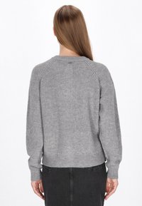 Pulover gri tricotat cu o textură ribbed, umeri raglan și un decolteu larg. Bază scurtă, ajustată la talie.