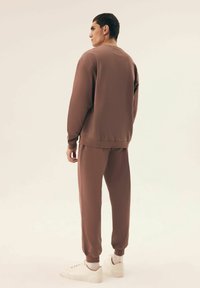 Brązowy zestaw odzieży sportowej składający się z lekkiego, fakturowanego swetra i dopasowanych spodni, uzupełniony białymi sneakersami.
