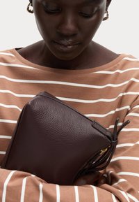 Donker bordeauxleren tas met een gestructureerd oppervlak, dicht tegen een gestreepte bruine top gehouden, met een ritssluiting en trekkoorddetail.