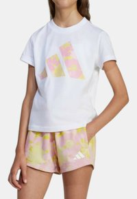 T-shirt bianco in cotone con grafica floreale rosa e gialla e logo. Abbinato a pantaloni corti rosa con motivo floreale e logo.