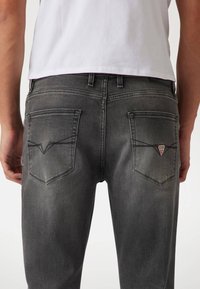 Vaqueros de mezclilla gris con una textura suave, que cuentan con dos bolsillos traseros y un pequeño logo de triángulo rojo en el bolsillo derecho.