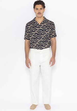 Korte mouwen shirt in marineblauw met een beige abstract patroon, gecombineerd met een witte broek en lichtbruine instapschoenen. Eenvoudig ontwerp en comfortabele pasvorm.