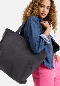 Grijze corduroy schoudertas met dikke schouderbanden. Voorzien van een logo aan de voorkant, gecombineerd met een spijkerjack en roze corduroy broek.