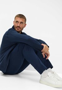 Marineblaues langärmliges Zip-Up-Oberteil, kombiniert mit passender Hose und weißen Sneakers. Verfügt über ein elegantes Design und einen weichen Stofftextur.